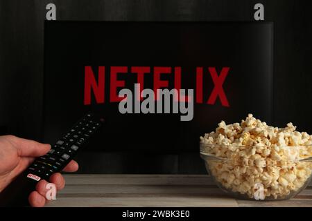 Nikolaev, Ukraine - November 20, 2021. Man with TV remote control in hand and Netflix logo in background. Netflix is the global provider of streaming Stock Photo