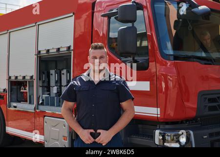 A confident firefighter strikes a pose in front of a modern firetruck, exuding pride, strength, and preparedness for emergency response Stock Photo