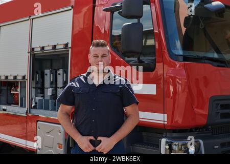 A confident firefighter strikes a pose in front of a modern firetruck, exuding pride, strength, and preparedness for emergency response Stock Photo