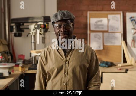 Portrait of kind Black senior craftsman wearing protective glasses and smiling at camera in workshop Stock Photo