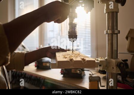 Close up of unrecognizable carpenter drilling wood using machine tool in workshop with sunlight Stock Photo