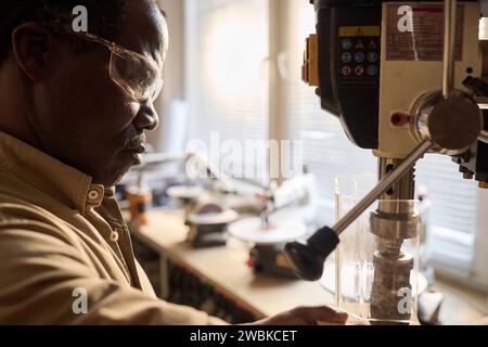 Side view closeup of Black man in protective glasses using machine tools in carpenters workshop Stock Photo
