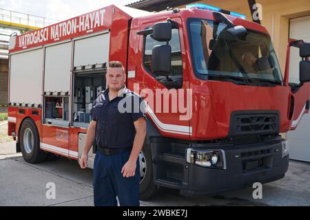 A confident firefighter strikes a pose in front of a modern firetruck, exuding pride, strength, and preparedness for emergency response Stock Photo