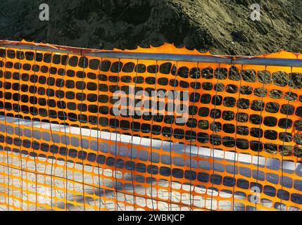 orange construction safety net in roadwork site with pile of soil in background Stock Photo