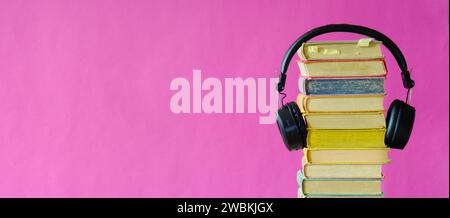 Relaxing with audiobooks concept with heap of books and vintage headphones.Bright pink background with large copy space Stock Photo