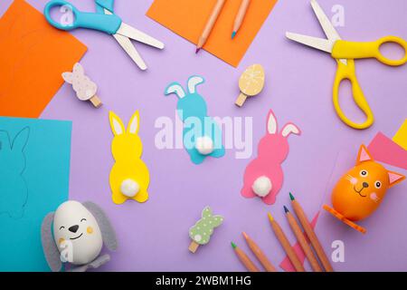 Easter bunnies handmade from colored paper, easy crafts for kids on purple background. Top view. Stock Photo