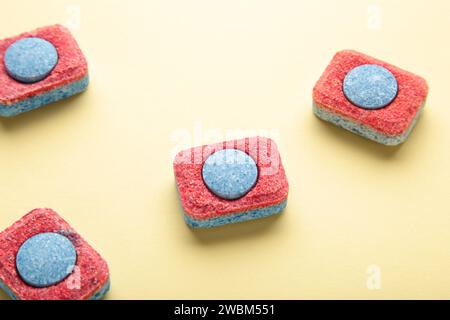 Red and blue tablets for dishwashing machine. Detergents for home hygiene. Dishwasher capsules on yellow background. Top view Stock Photo