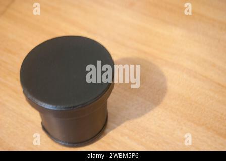 Black dice cup, with lid on, on wooden desk Stock Photo