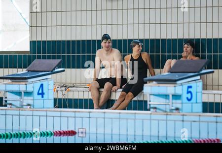 Young woman and men swimming club teammates sitting at the pool and talking Stock Photo