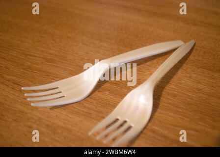 Two white plastic forks on a wood grain surface Stock Photo