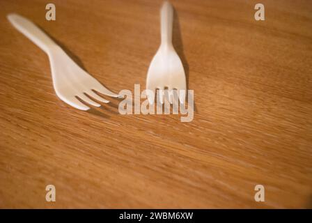Two white plastic forks on a wood grain surface Stock Photo