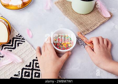 Sweet flavors of Easter vibes, child adds sprinkles to decorate cookies top view. Stock Photo