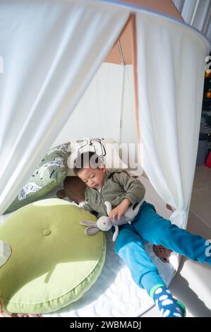 Adorable two and a half little boy is playing with soft toy rabbit in a white kids tent. Boy having fun as he sails through a fantasy world with his s Stock Photo