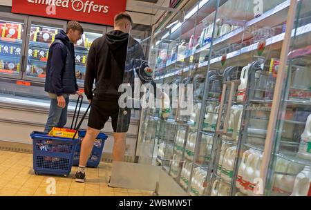 Young men students male shoppers people rear back behind view looking at milk on shelves shopping in Lidl supermarket Great Britain UK  KATHY DEWITT Stock Photo