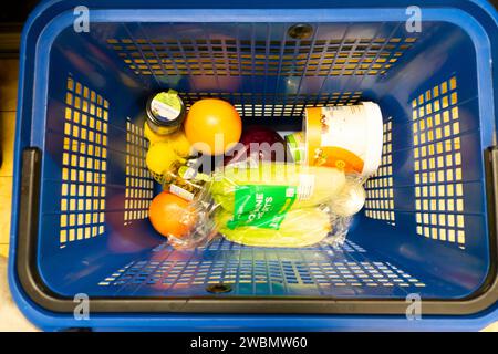 View from above looking down on few food items in blue plastic shopping basket at Lidl supermarket waiting checkout counter queue 2024 UK KATHY DEWITT Stock Photo