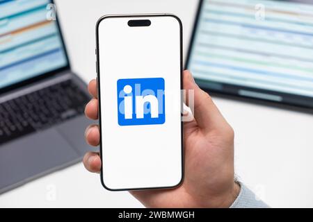 LinkedIn logo of social media application on the screen of smart phone in mans hand, laptop and tablet on the background Stock Photo