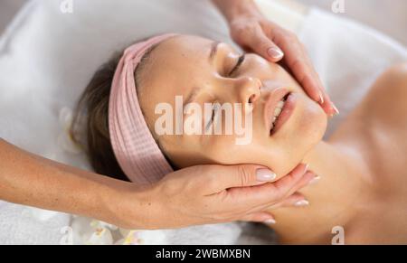Young female client receiving soothing and relaxing facial massage Stock Photo