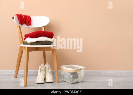 Stack of folded sweaters with gloves on chair and boots near beige wall Stock Photo