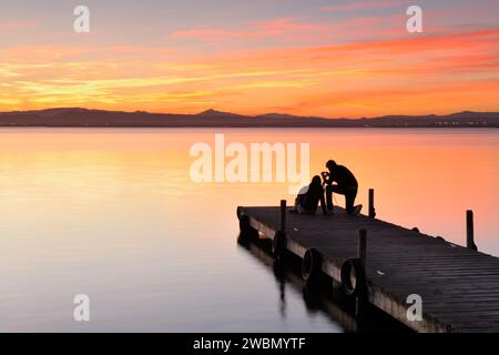 Backlit silhouettes of two people taking pictures of a wonderful sunset over the walkway of the Albufera lake in Valencia, Spain. Stock Photo