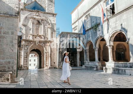 A stylish woman strolling confidently along a charming brick road, flanked by towering buildings Stock Photo
