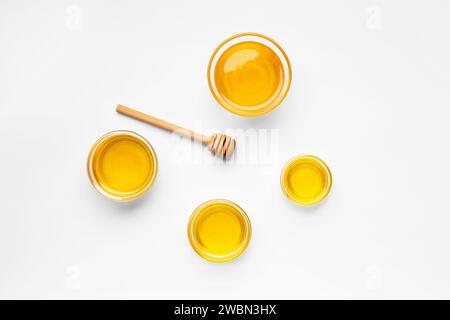 Creative composition of honey in glass bowls of different sizes and a wooden dipper on a white background top view. Organic honey and honey spoon Stock Photo