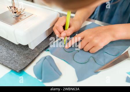Close up of female hands working on sewing machine. She is sitting at the table and drawing with green pencil. Creative tailoring workshops for childr Stock Photo