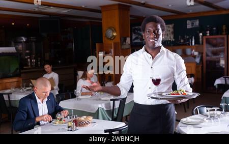 Hospitable african american waiter greeting guests in restaurant Stock Photo