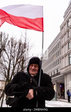 Warsaw, Poland, 11th of January 2024. An elderly man holds Polish national flag during a protest against changes in public media in Poland and in protection of democracy - Law and Justice party (Prawo i Sprawiedliwość) politicians say. Law and Justice party ruled in Poland for 8 years until they lost last election in October 2023. The party now become mayor a right-wing opposition force against more centrist and liberal ruling coalition, where the main political force is Civic Coalition lead by Donald Tusk, former President of the Council of EU and now Prime Minister of Poland. Credit: Dominik Stock Photo