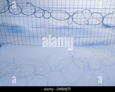 Barbed, razor wire - some coils of barbed wire razor fence, and its shadow on snow Stock Photo