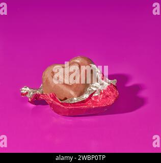 A Piece of Foil Covered Valentine's Day Milk Chocolate Candy on a Bright Pink Background Stock Photo