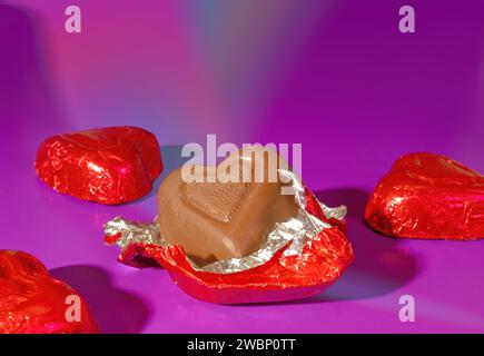 Four Pieces of Red Foil Covered Valentine's Day Milk Chocolate Candy on a Bright Pink Background Stock Photo