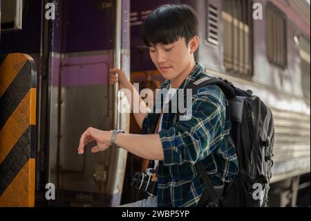 A handsome young Asian man traveler is checking time on his wristwatch while getting off the train, checking the arrival time. Stock Photo