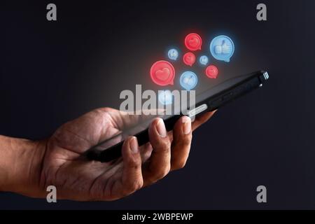Hand holding smartphone and glowing heart and thumbs up icon. Social media concept. Stock Photo