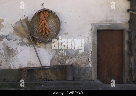 Wall of a rural house in Slovenia with farming tools and ears of corns drying. Stock Photo