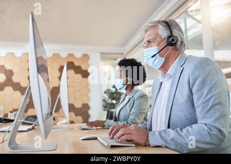 Covid, call center employees with mask at computer and senior man with black woman in headset. Office compliance, consulting team online in shared Stock Photo