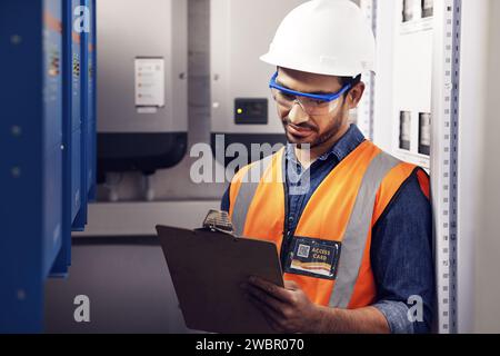 Man, electricity and technician in control room, writing notes and machine maintenance on clipboard. Male electrician, system and electrical Stock Photo