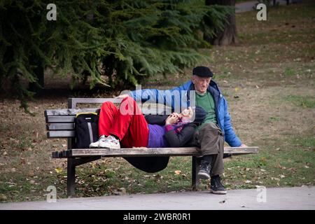 Middle age senior couple enjoying nice autumn sunny day at the bench in public city park Stock Photo