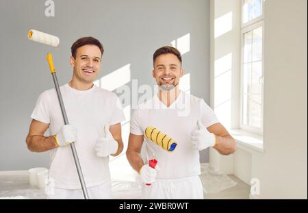 Team of house painters looking at camera with paint rollers and showing thumb up sign. Stock Photo