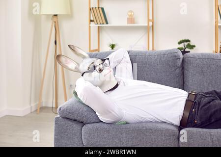 Funny man wearing in a rabbit animal mask lying on couch at home or in office resting. Stock Photo