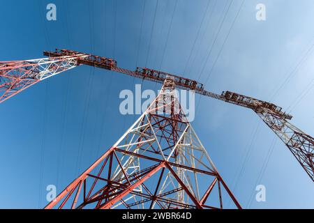 Tall electrical masts for transmitting high voltage current from a power plant against a blue sky, shot with an ultra-wide angle lens from a low point Stock Photo