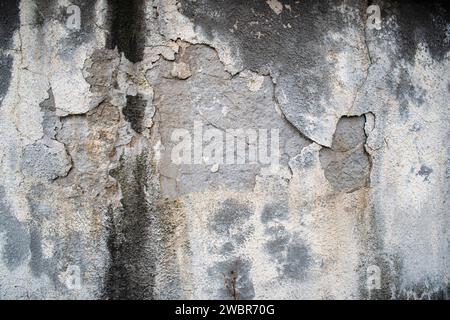 Cracked, peeled and damaged exterior wall plaster, gray, no people. Stock Photo