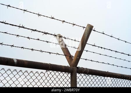 Barbed wire fence set against gray winter sky, no people. Stock Photo