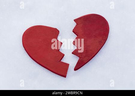Red broken in half toy heart in the snow, concept or metaphor broken heart, background for Valentine's Day Stock Photo