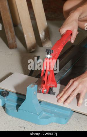Cutingt tiles with a standard manual tile cutter. Process of installation of tiles in the bathroom step by step. DIY home improvement. Stock Photo