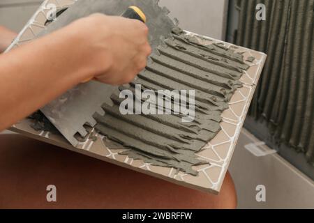 Woman tiling bathroom walls, applying adhesive on a tile and placing ceramic tile in right position. Process of installation of tiles in the bathroom Stock Photo