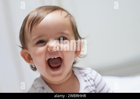 Baby girl, funny and happy for playing, child development and infant growth with face, sitting and home. Laugh, joyful and healthy in good mood Stock Photo