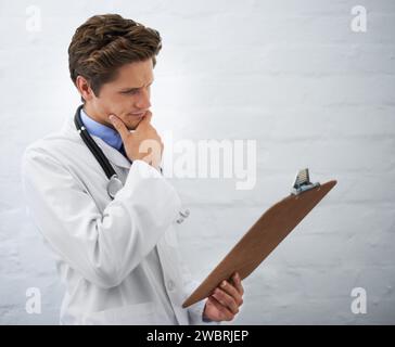 Clipboard, thinking and man doctor in office for reading or brainstorming for diagnosis treatment. Ideas, checklist and professional young male Stock Photo