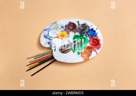 Painter palette with multiple smudged colors and brushes on beige background, abstract Stock Photo