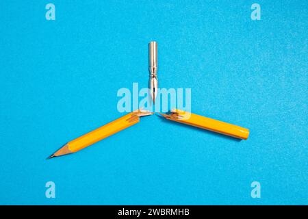 Vintage pen nib breaking a crayon in half, on blue paper background concept Stock Photo