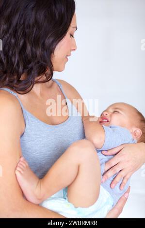 Mom holding toddler in home with crying, comfort and child care with support in morning. Happy woman, tired baby boy and nap time together in bedroom Stock Photo